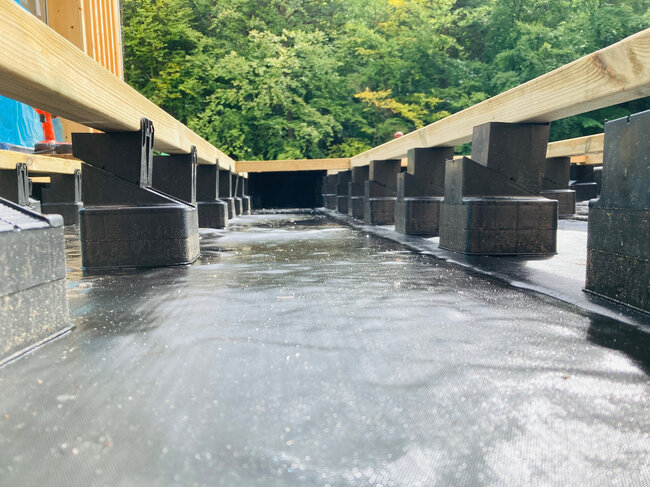 Plots de terrasse en plastique réglables supportant des lambourdes en bois sur une membrane de toiture imperméable.