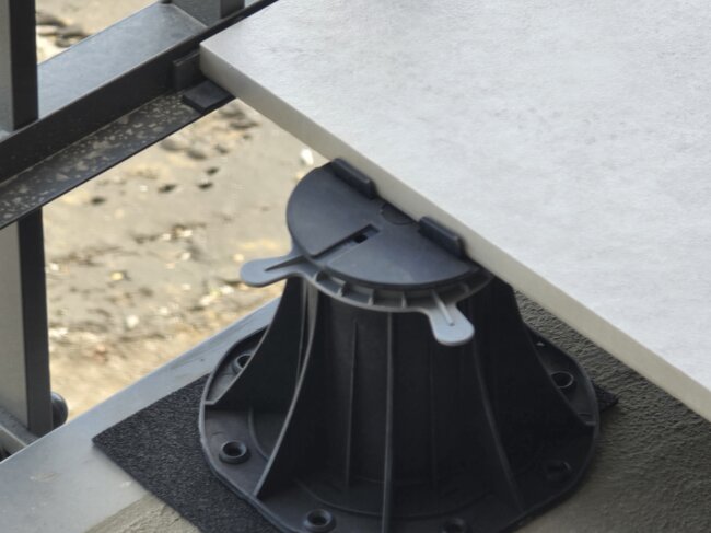 Plot réglable supportant le bord d'une dalle en porcelaine extérieure sur un balcon.