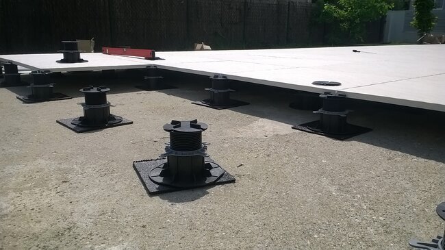 Installation d'une terrasse surélevée à l'aide de plots réglables pour supporter de grandes dalles de terrasse en porcelaine.