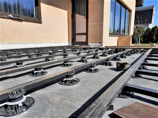 Plots réglables de terrasse supportant une sous-structure à lambourdes métalliques pour la pose de lames composites.