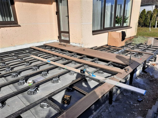 Pose de lames de terrasse composite sur une sous-structure de lambourdes supportée par des plots réglables.