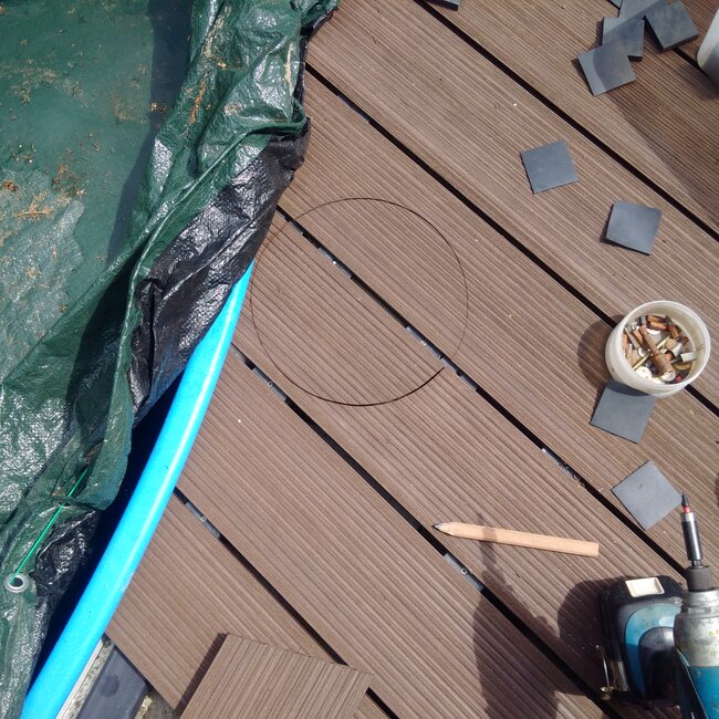 Marquage et découpe des lames de terrasse composite autour des bords de piscine sur un système de plots réglables.